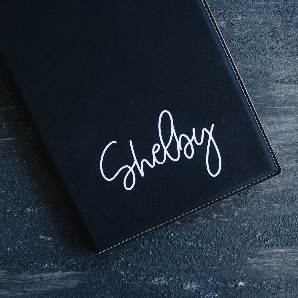 Close-up of black note pad holder cover with 'Shelby' cursive print