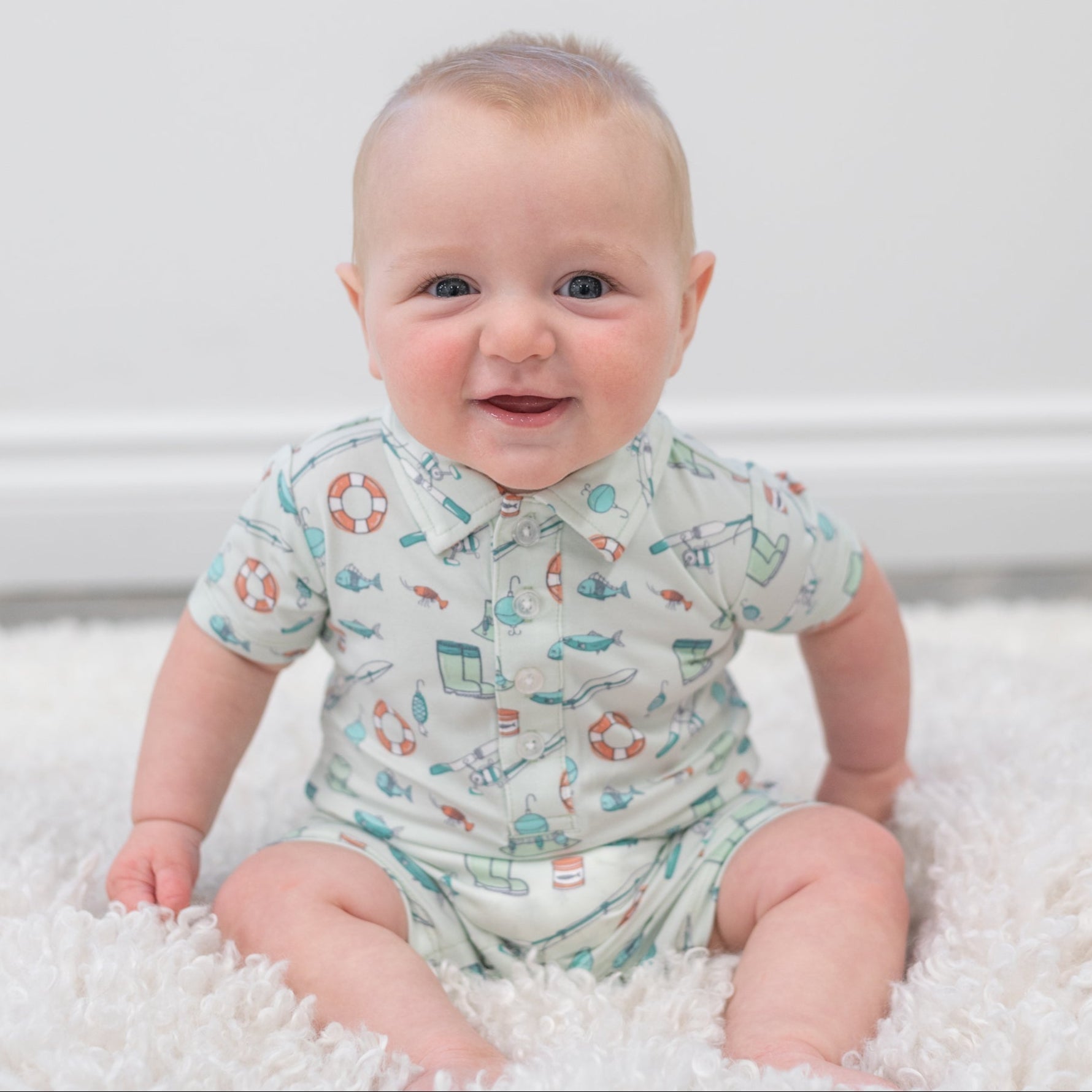 Infant fishing polo romper in light cream with teal and orange fishing motifs, button front