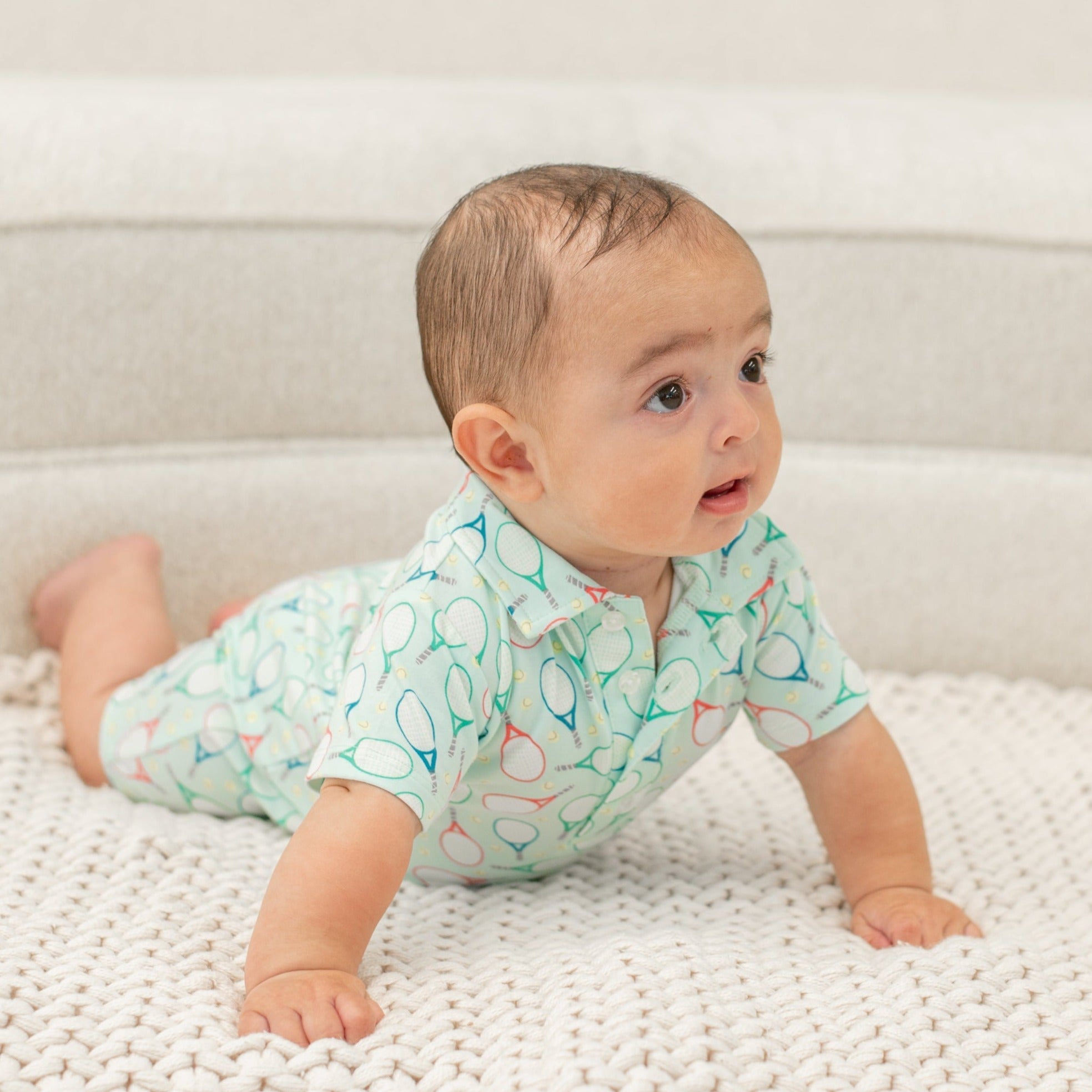 Turquoise polo romper for boy, short sleeves, button collar, tennis racket pattern.