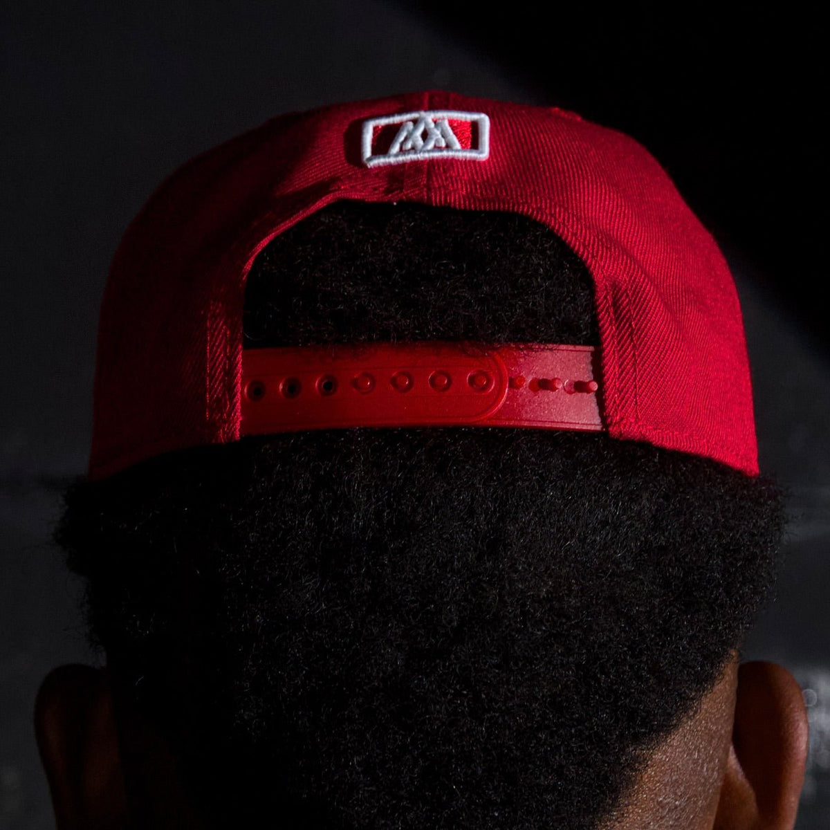 Red snapback cap back with white square patch and adjustable strap holes