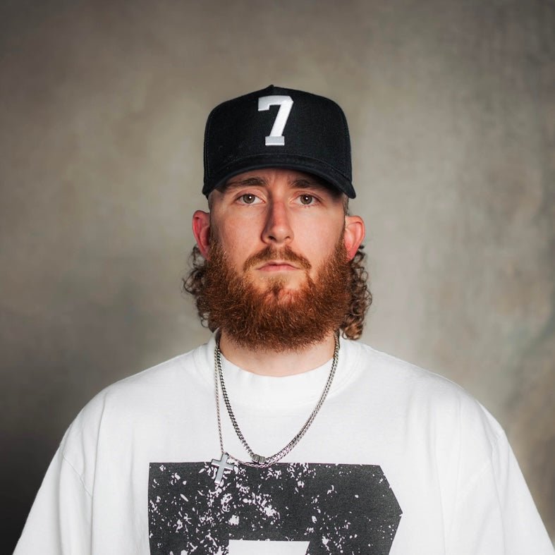 Black snapback cap with white '7' patch worn by bearded man