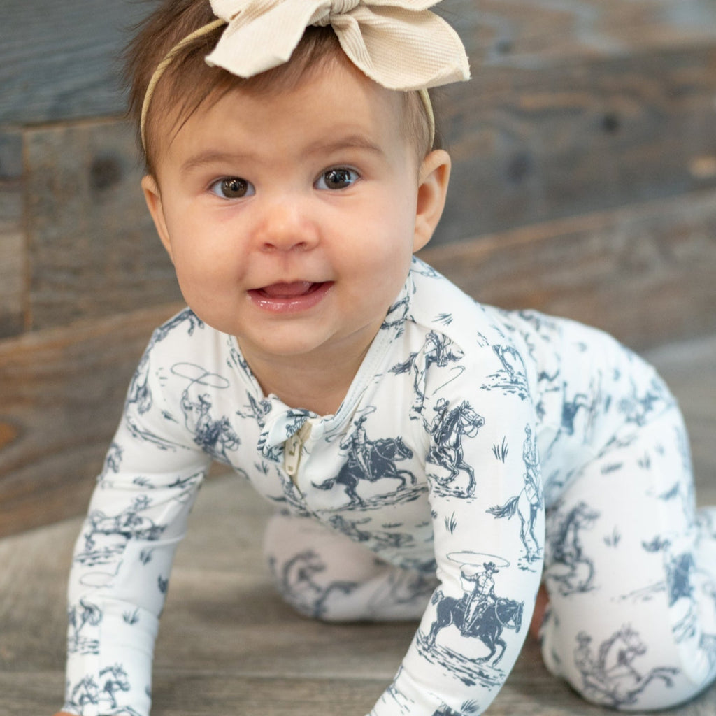 Baby long-sleeve romper with blue cowboy print on white background, worn close-up