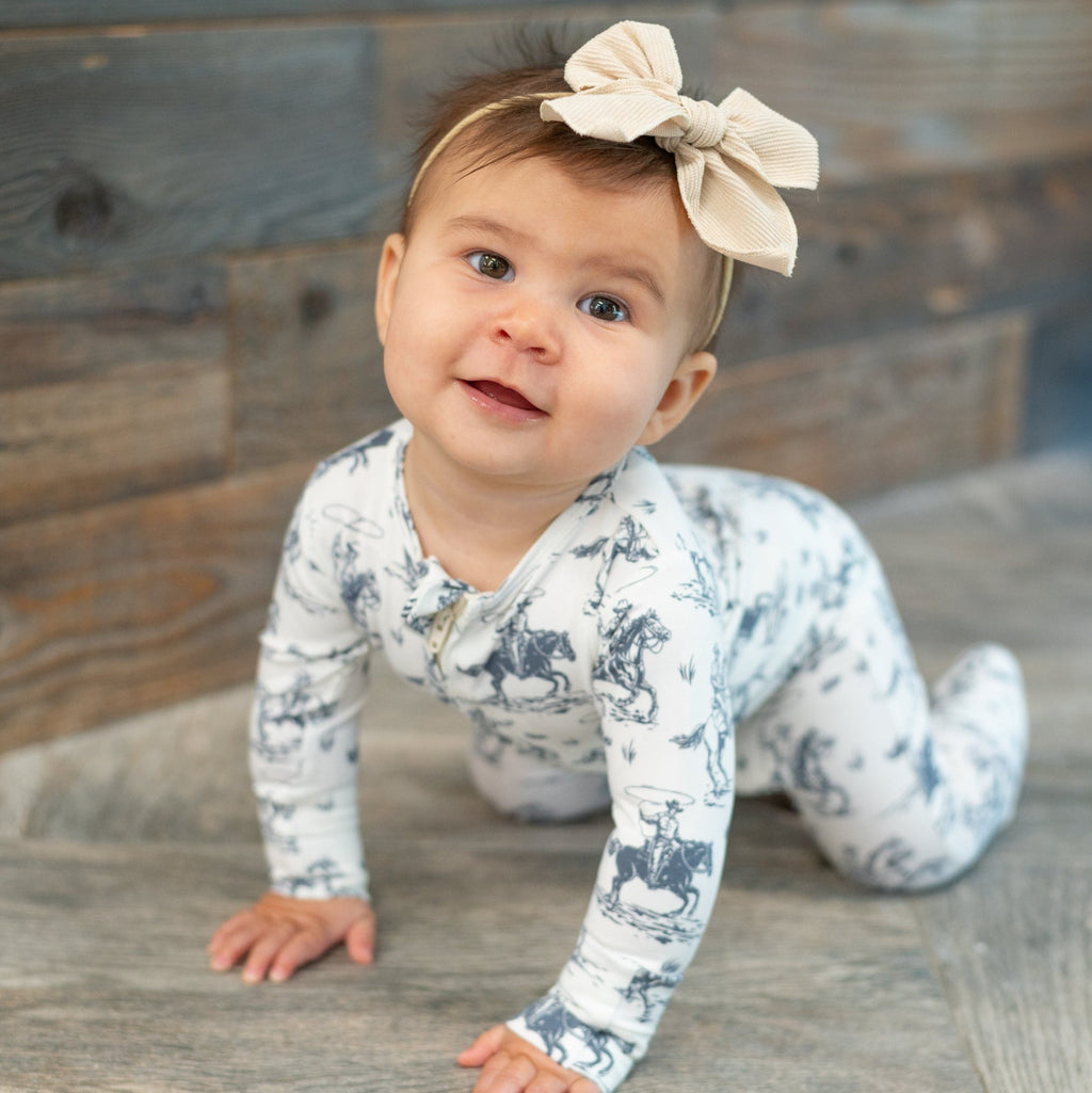 Baby long-sleeve romper with blue cowboy print on white background and footed legs