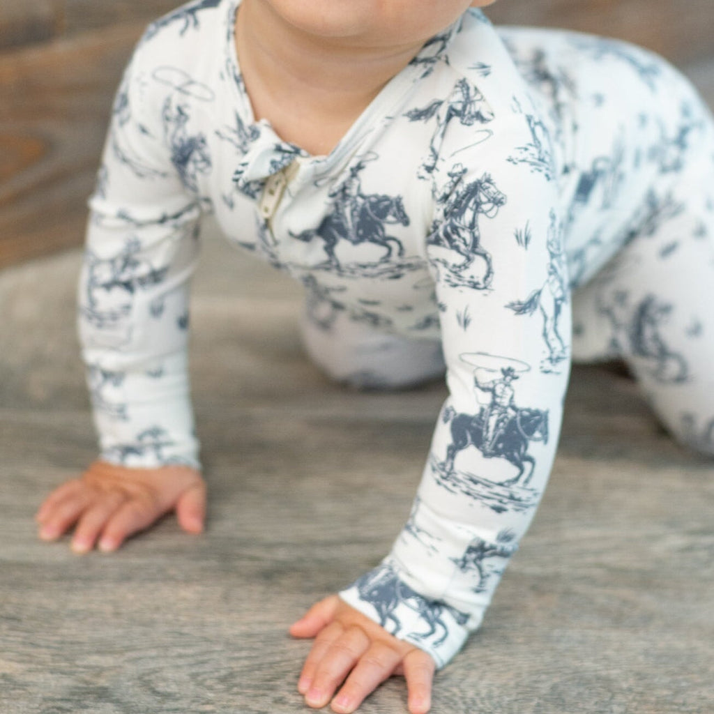White zip-front footie pajama with blue cowboy print, long sleeves, foldover cuffs