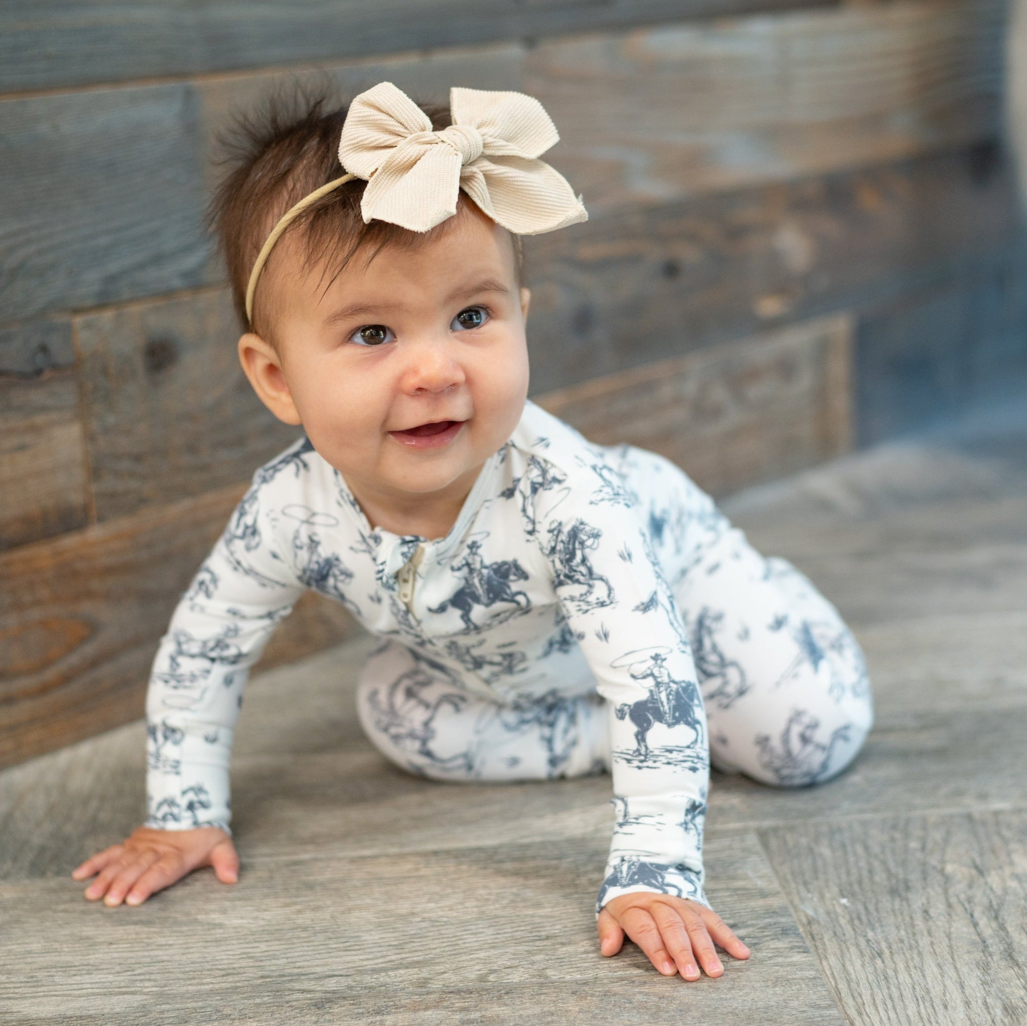 White cowboy-print zip-front footie worn by baby crawling, long sleeves and cuffs