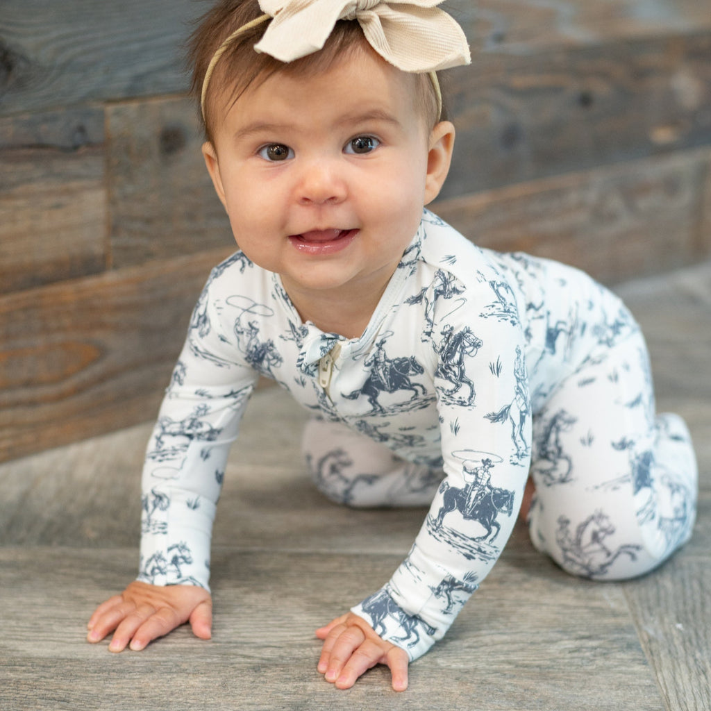White cowboy-print zip-front footie worn by baby, long sleeves and ankle cuffs