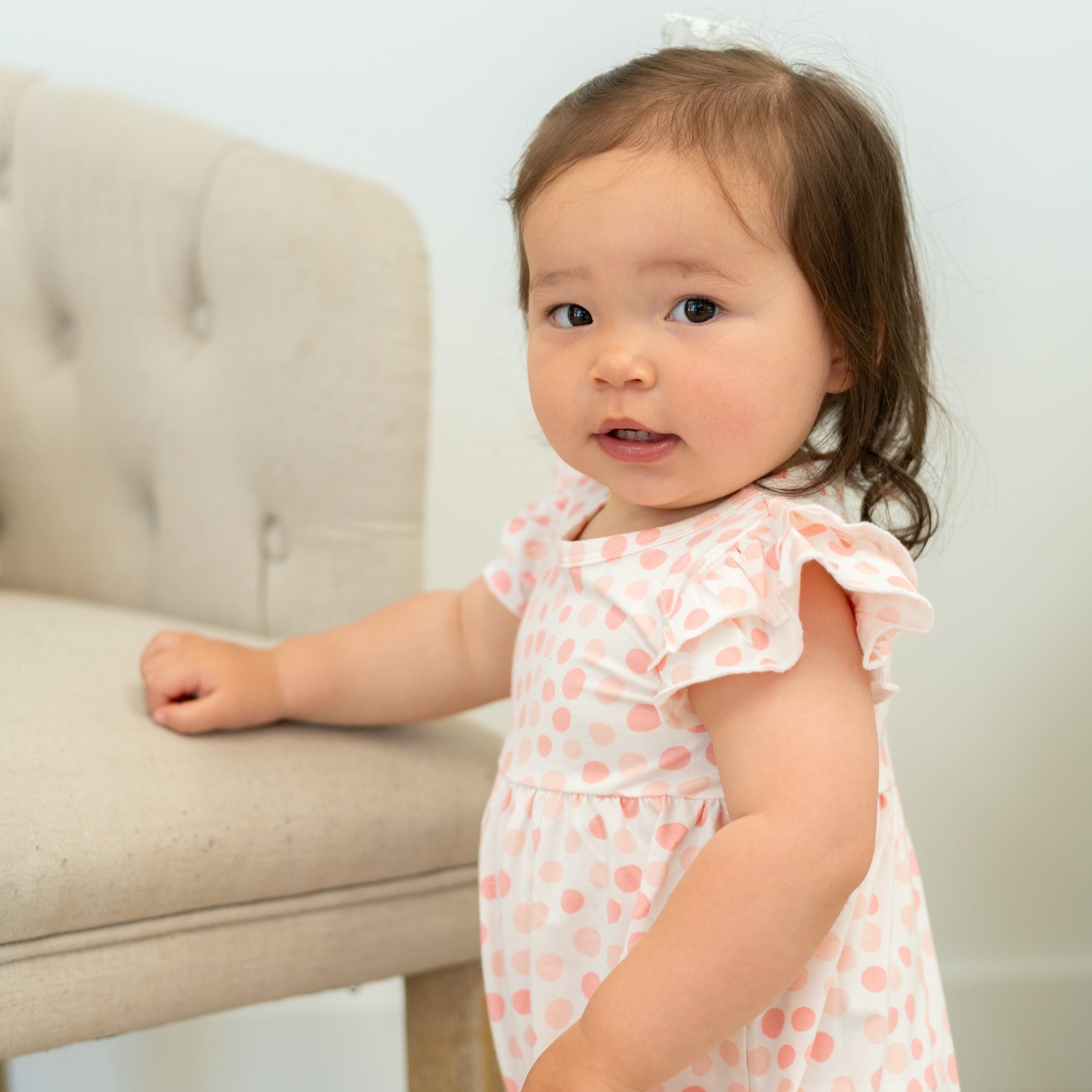 Baby girl in pink-and-white polka dot ruffle romper with frilled flutter sleeves