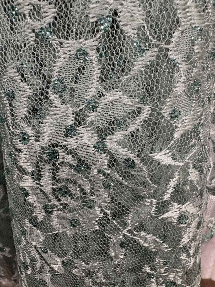 Lace fabric close-up with textured floral mesh pattern, silver and teal tones