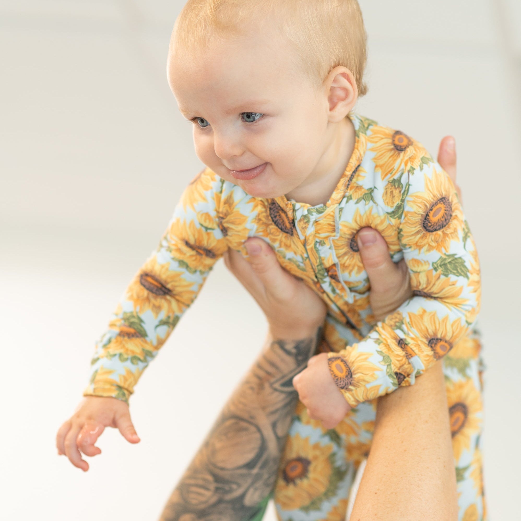 Sammy's sunflower ruffle footie with long sleeves and button front, worn by a baby girl