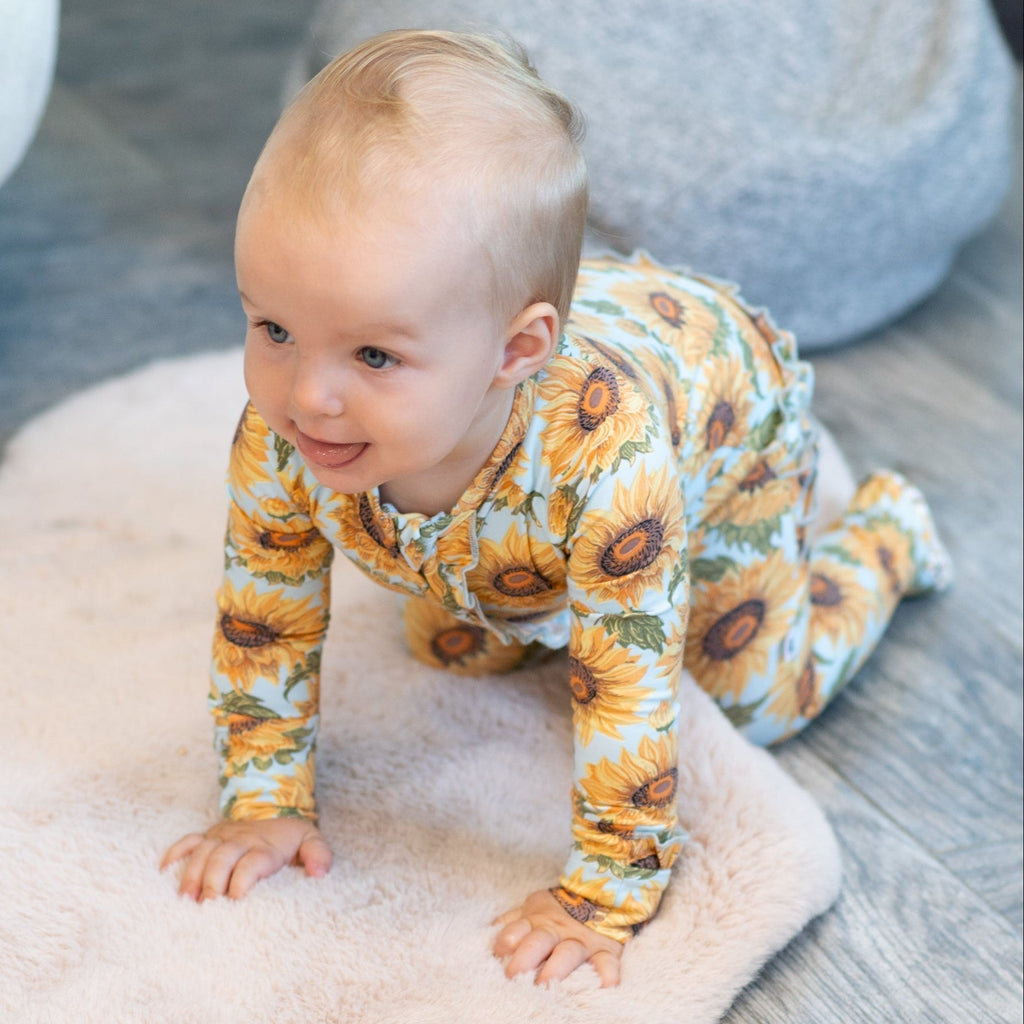 Sunflower ruffle footie with long sleeves and button placket, worn by a baby girl