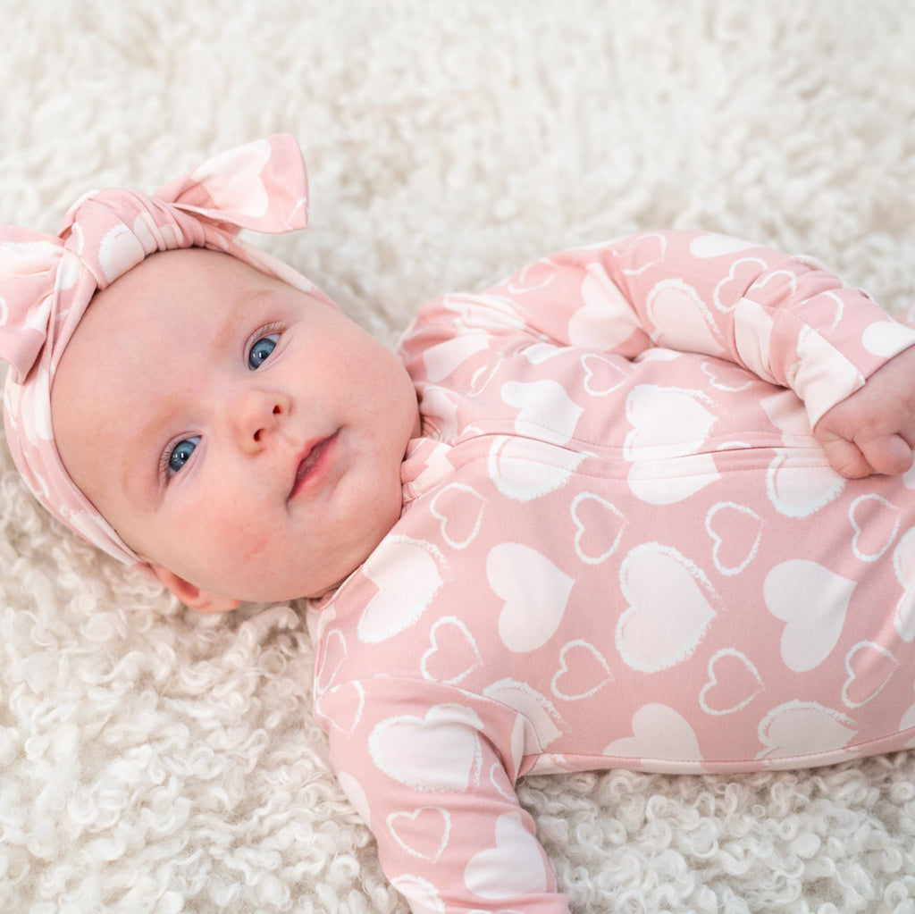 Pink heart-print convertible romper with long sleeves and front zip, worn with bow headband
