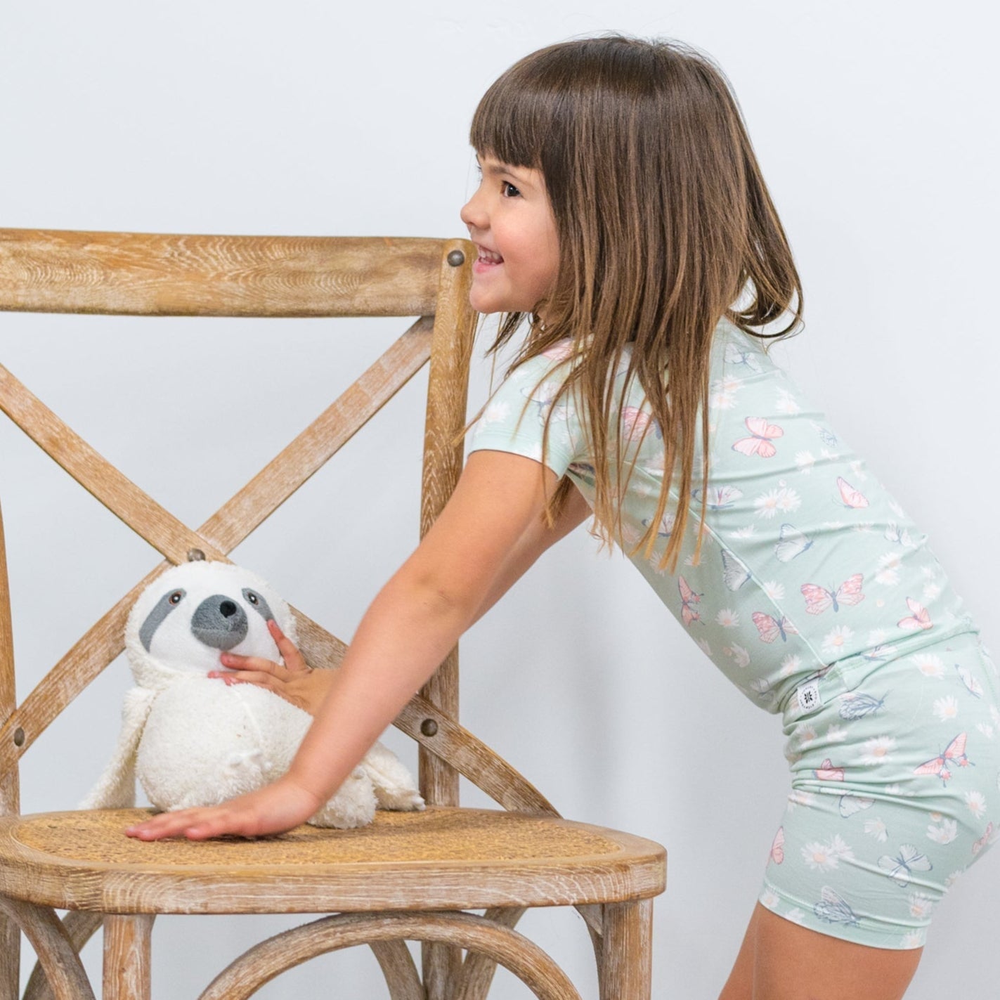 Girls mint pajama set with short sleeves and shorts, leaning forward on a wooden chair
