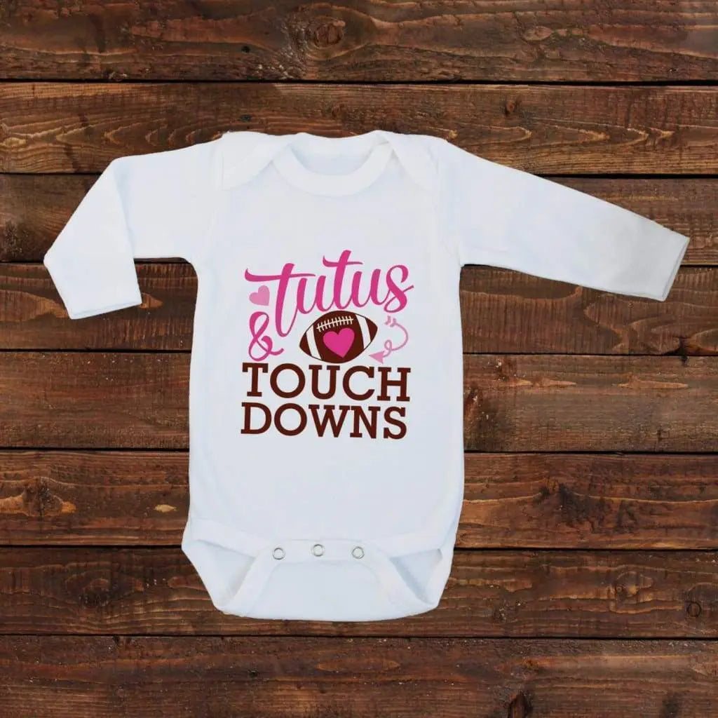 White long-sleeve baby bodysuit with 'Tutus & Touch Downs' pink text, heart, snap