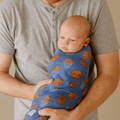 Blue basketball hoop swaddle blanket with hoop and ball pattern, worn on baby.
