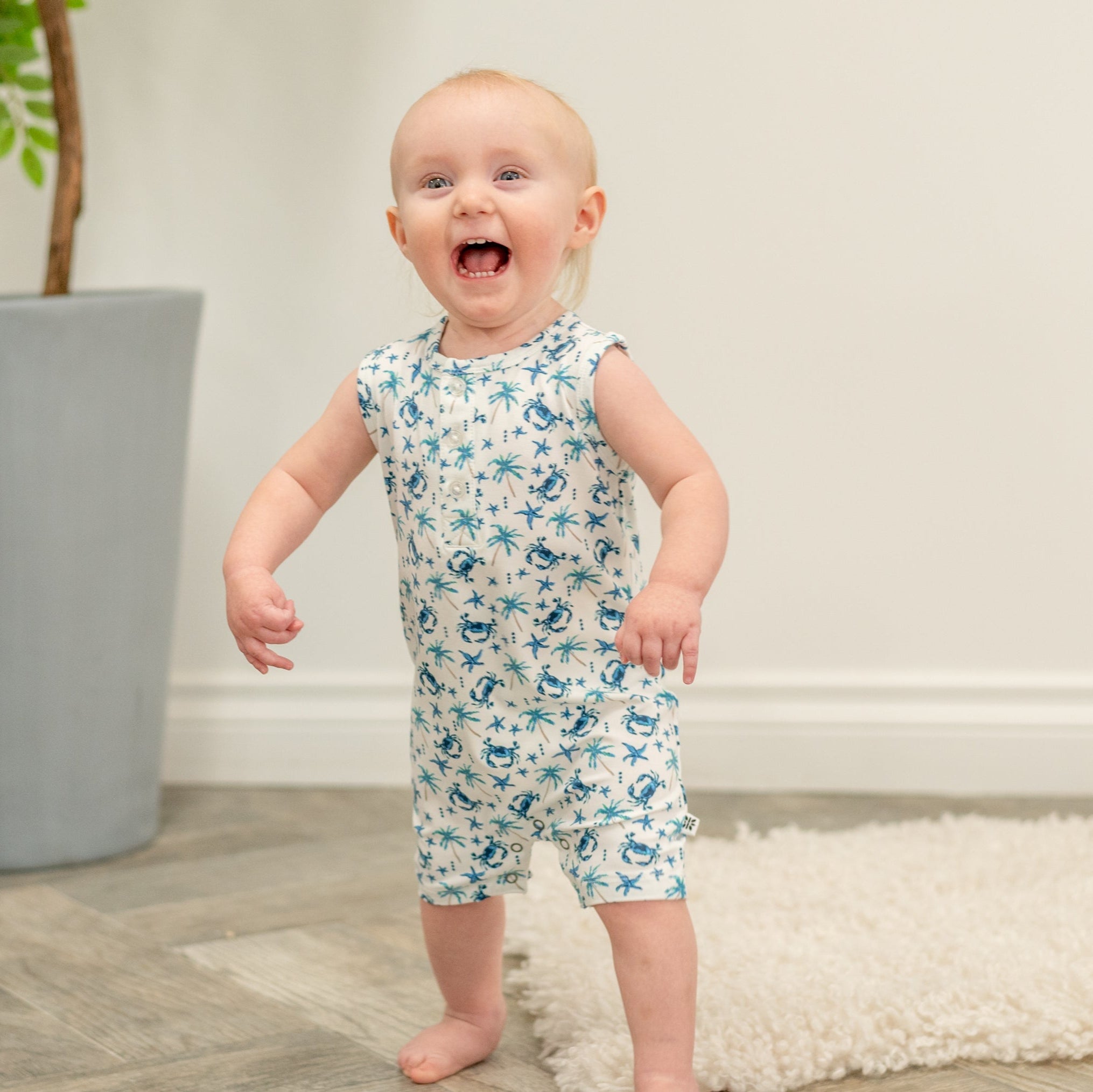 Baby wearing white blue crab and palm print tank romper, full-body view