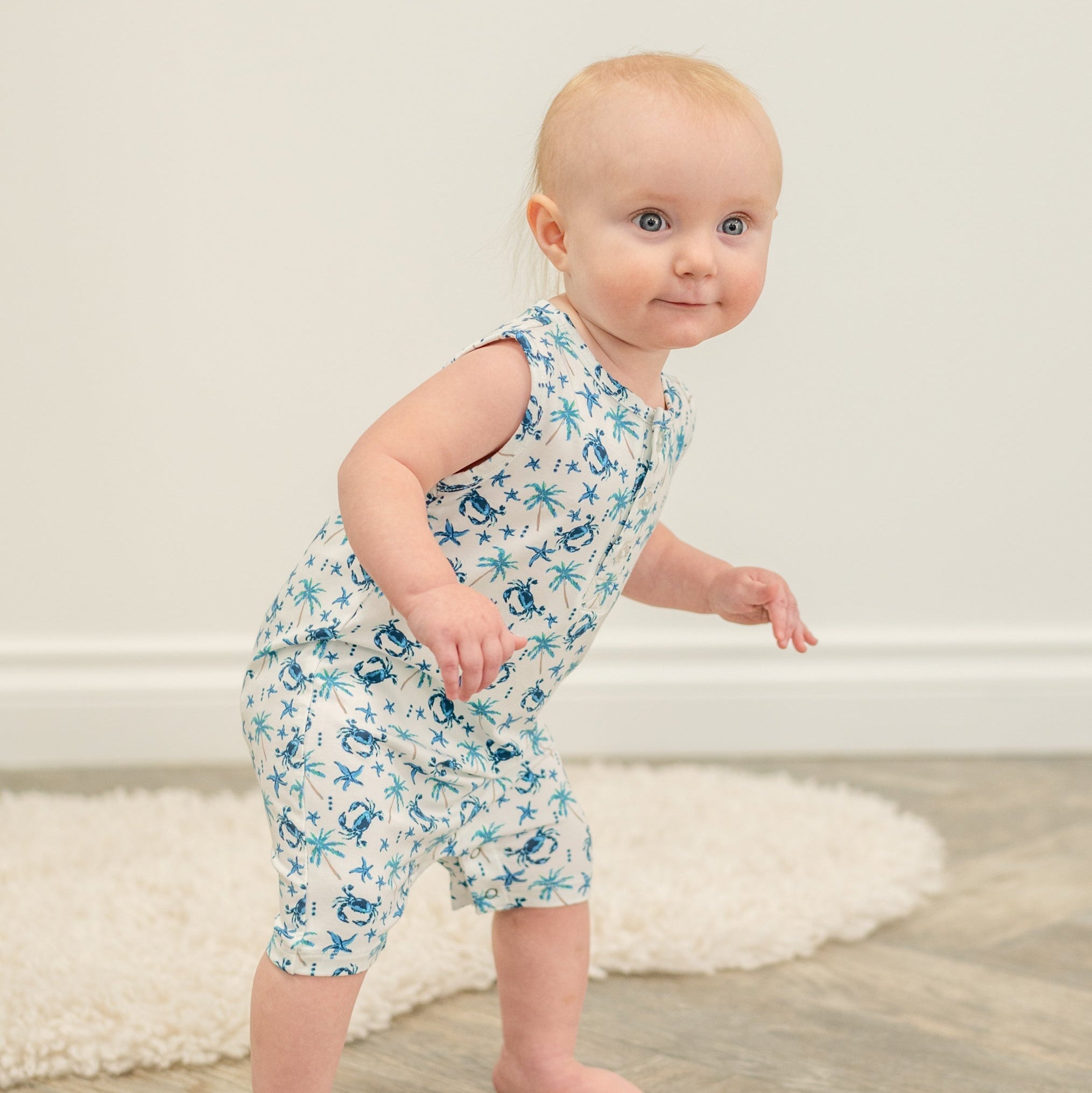 Baby in white blue crab and palm print tank romper, standing pose