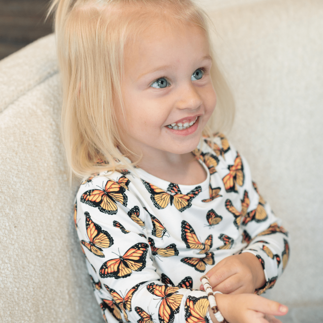 Child in kids pajama set, white long-sleeve with orange and black butterfly print