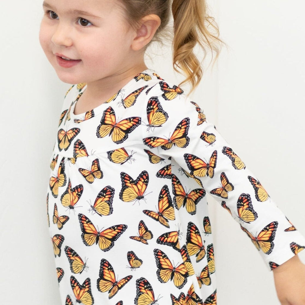 Girl's butterfly print dress close-up, white fabric with orange and yellow butterflies