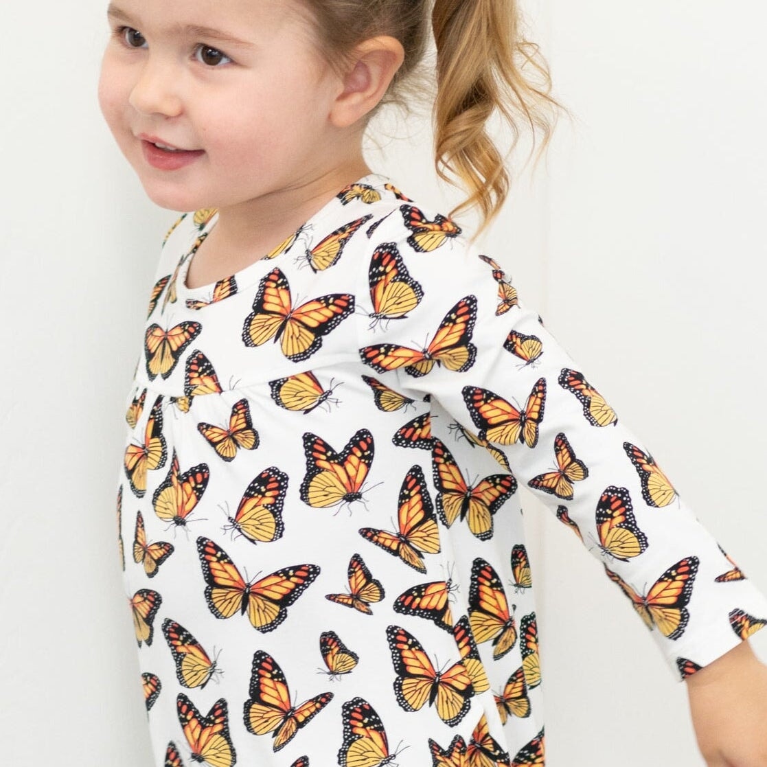 Girl's butterfly print dress close-up, white fabric with orange and yellow butterflies