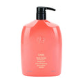 Oribe conditioner bottle, coral pink with black pump and circular emblem on front