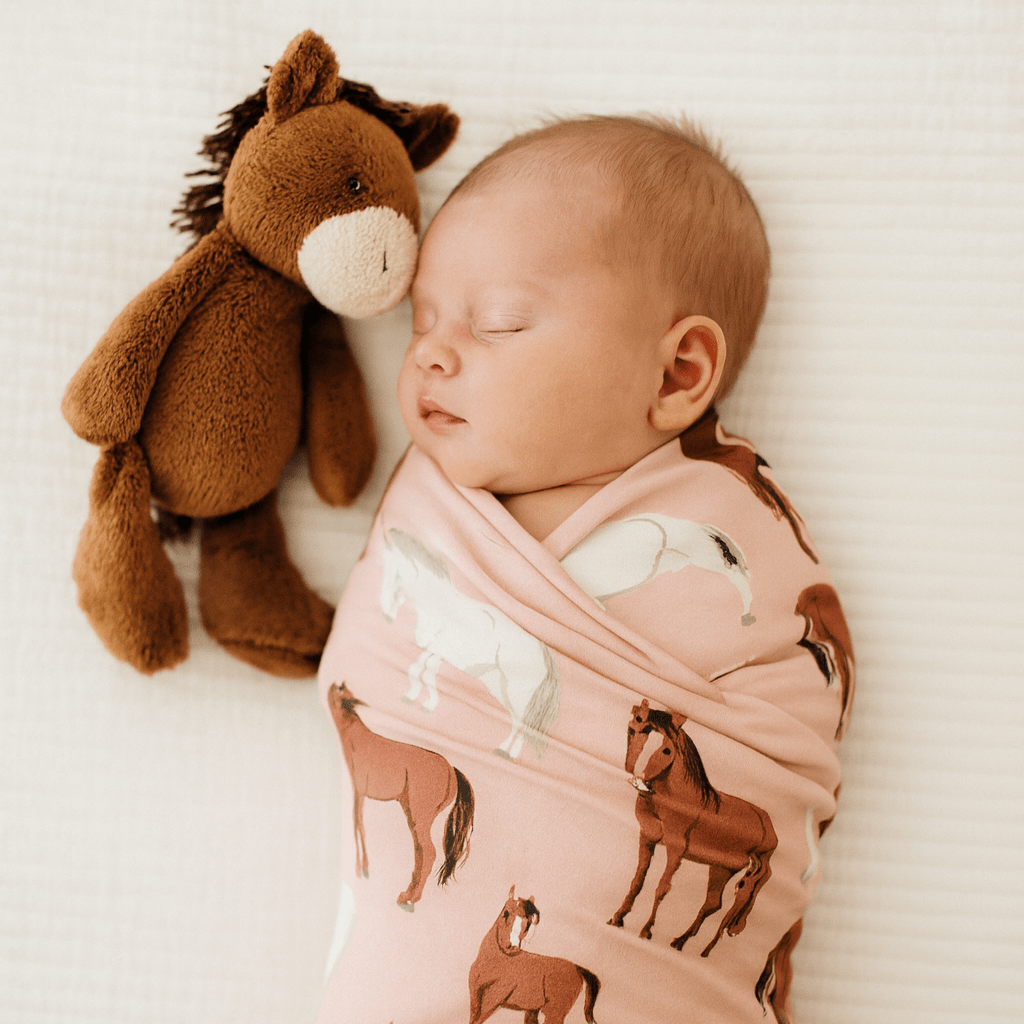 Horse-print swaddle blanket on a sleeping baby, light pink with brown wild horses