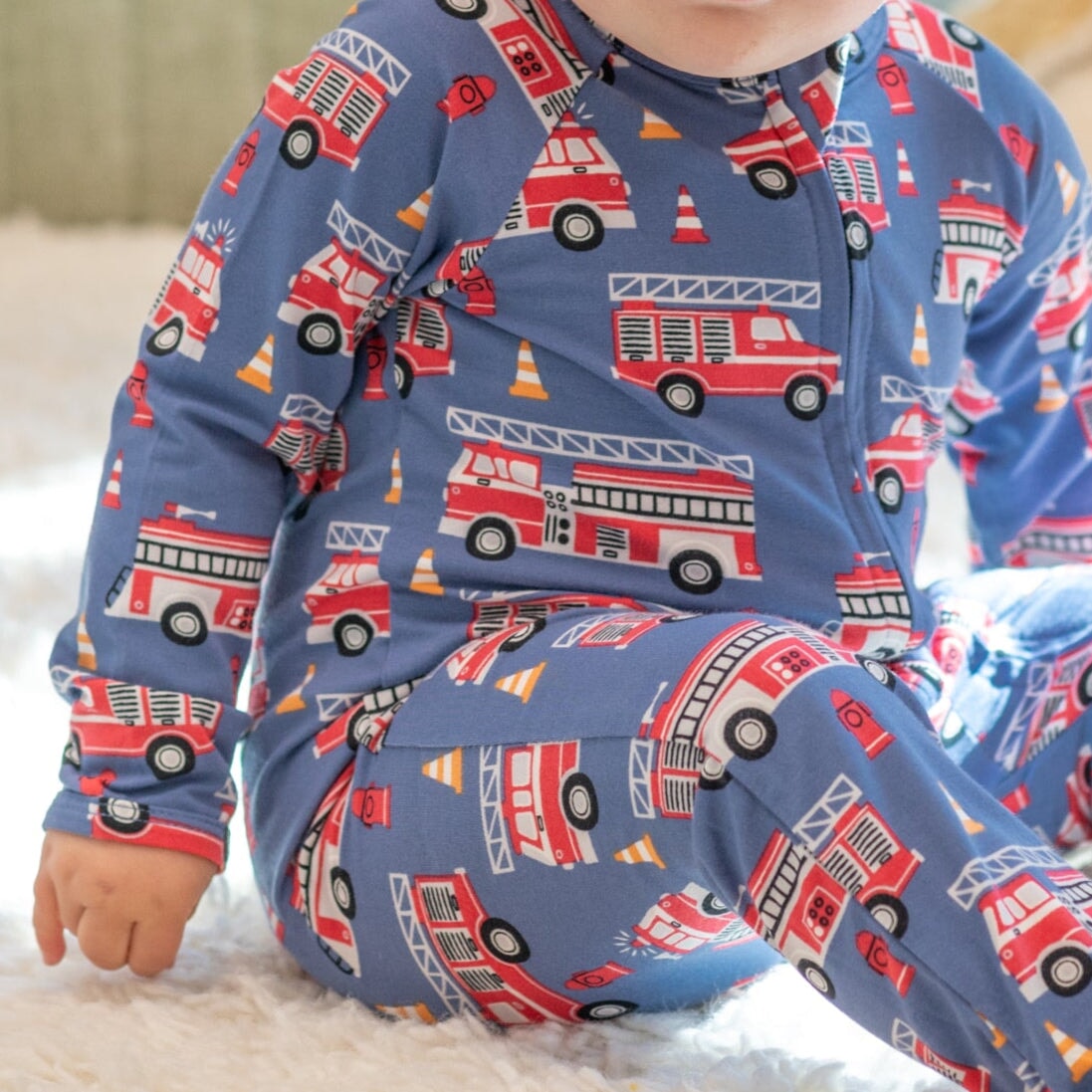 Blue fire truck zipper footie with red and yellow vehicle graphics, front close-up