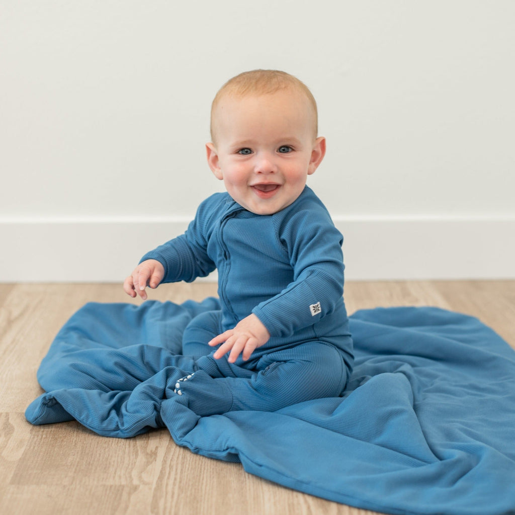 Blue zip-up footie pajama on smiling baby, long sleeves and front zipper